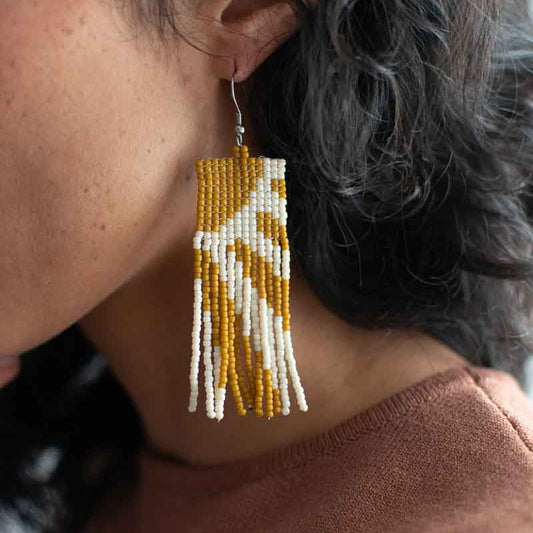 Close-up of a person wearing a beaded earring with yellow and white pattern.