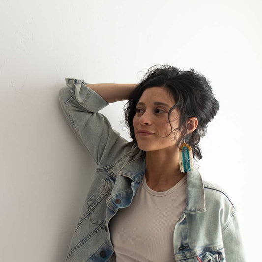 Woman wearing a light denim jacket and beige top against a white wall
