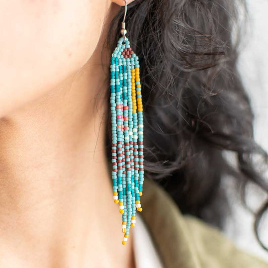 Close-up of a person wearing colorful beaded earrings with a blurred background