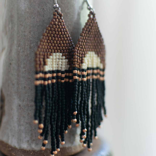 Beaded earrings with brown, black, and beige pattern on a textured surface.
