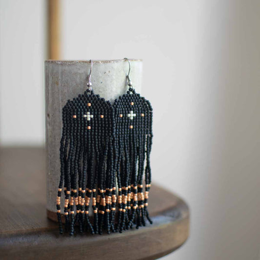 Black beaded earrings woven with gold accents on a wooden surface.
