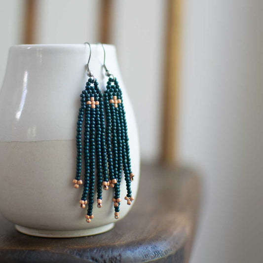 Beaded earrings hanging from a white cup on a wooden surface