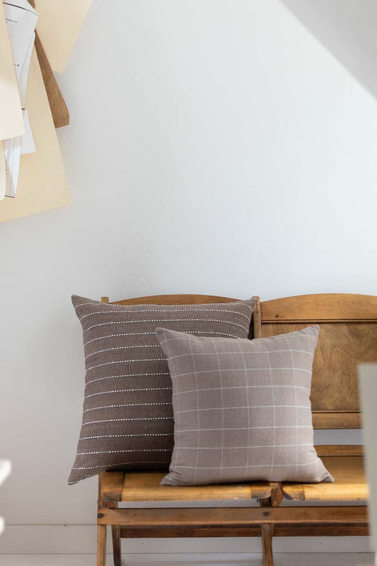 Two patterned cushions on a wooden bench against a white wall.