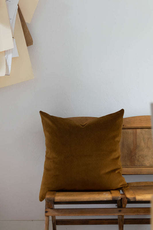 Brown pillow on a wooden bench against a white wall
