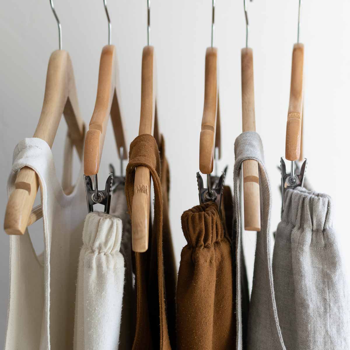 Pants and tops made from natural fibers hung on wooden hangers