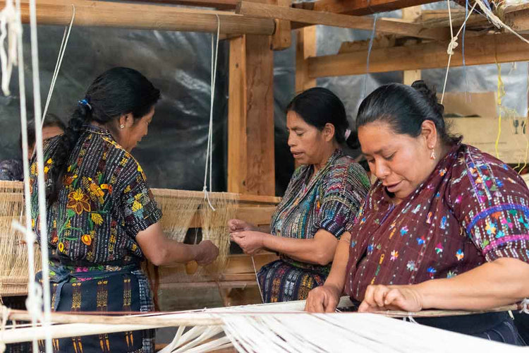 Three Kaqchikel women warp the floor loom to weave textiles.