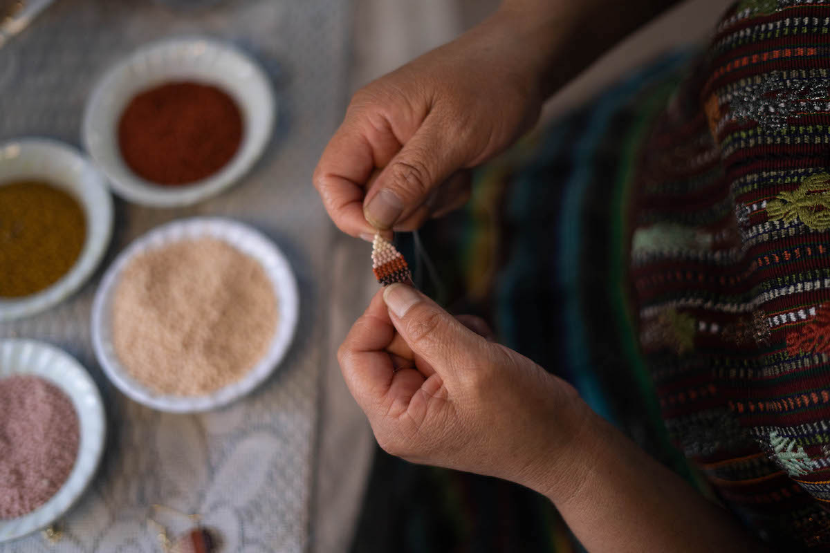 Two hands holding a pair of woven earrings to demonstrate beadwork.