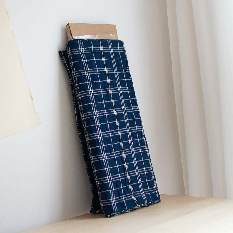 Handwoven blue Guatemalan plaid fabric on a wooden block against a white curtain background
