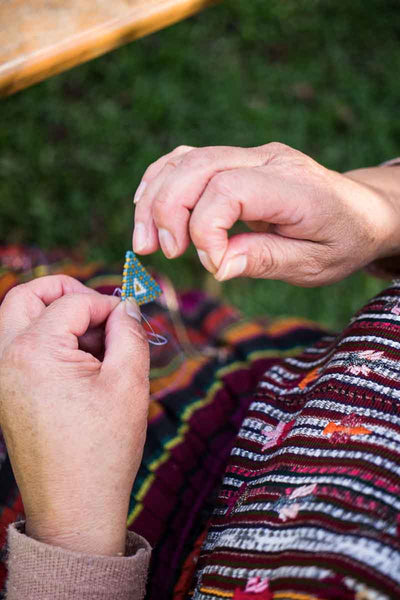 artisan weaving beaded earrings at a fair trade coop