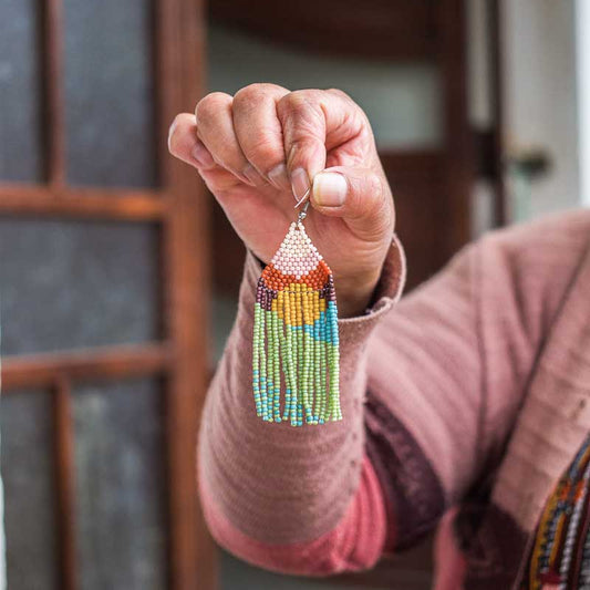 Artisan hand holding up a finished beaded earring that she made.