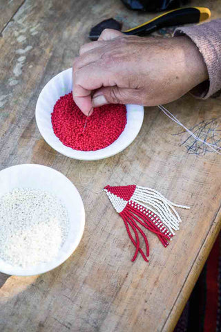 artisan weaving beaded earrings at a fair trade coop