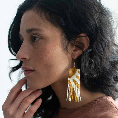Woman wearing gold and white beaded earrings against a neutral background