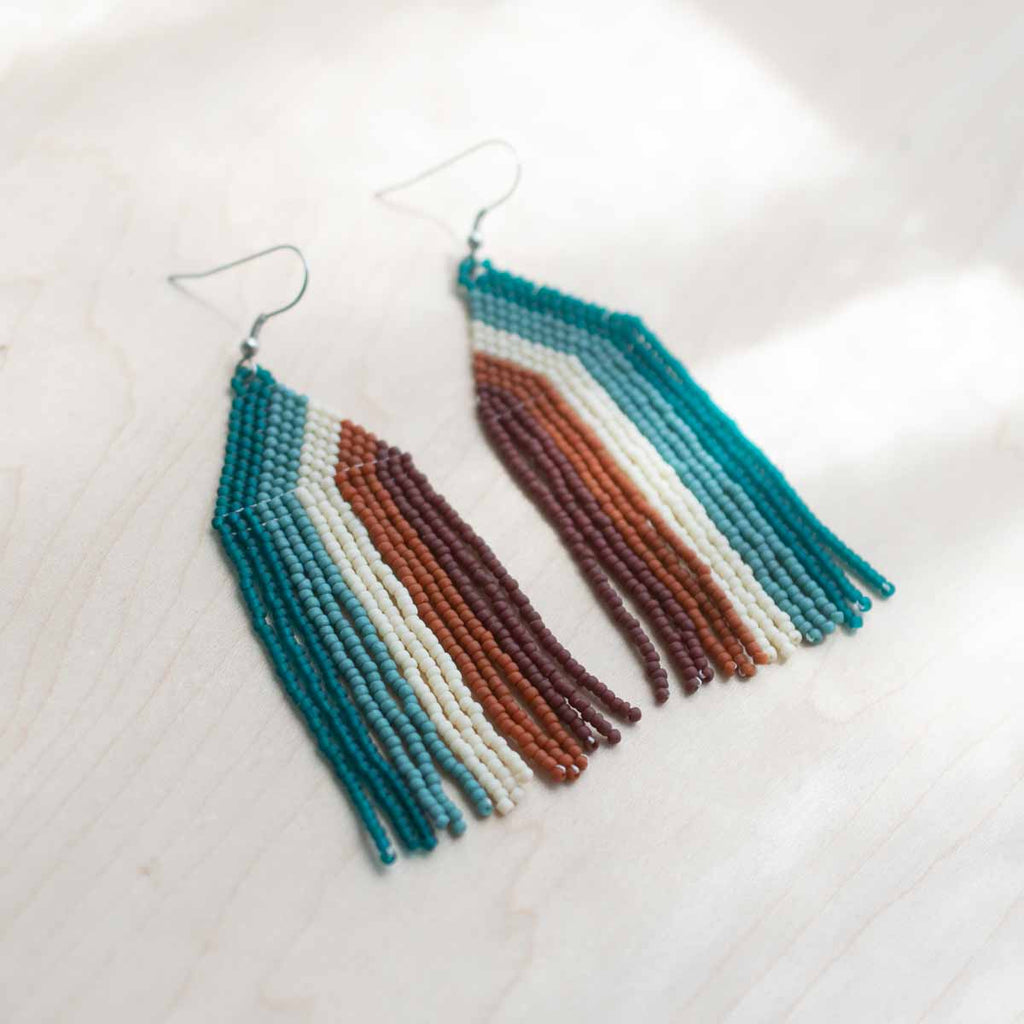 Beaded earrings with blue, brown, and beige fringes on a light background