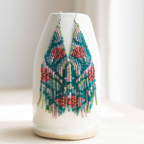Colorful beaded earrings on a white vase with a white background