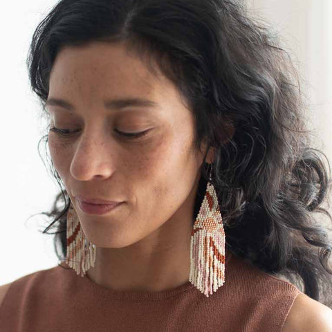Woman wearing long beaded earrings with a neutral background