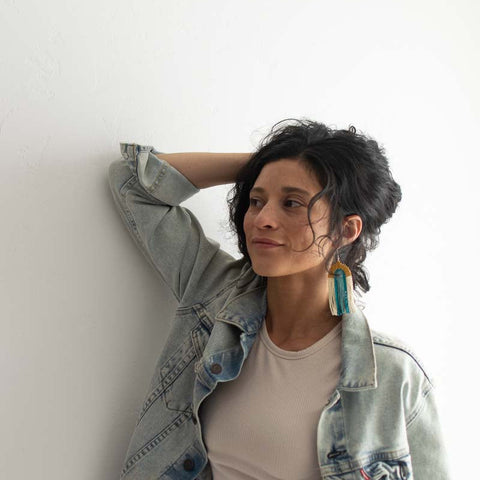 Woman wearing a light denim jacket and beige top against a white wall