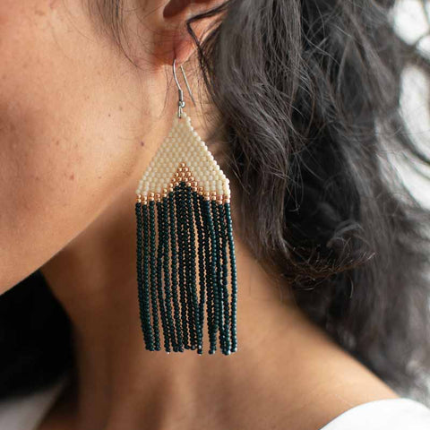 Close-up of a person wearing a beaded earring with green and gold beads.