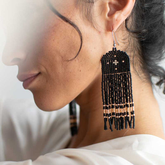 Close-up of a woman wearing black beaded tassel earrings against a neutral background
