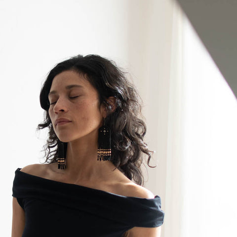 Woman wearing a black off-shoulder top with long black and gold eaded earrings