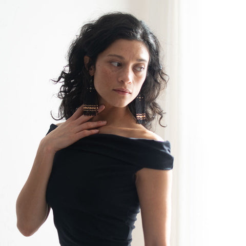 Woman wearing a black off-shoulder top and long black and gold tassel beaded earrings