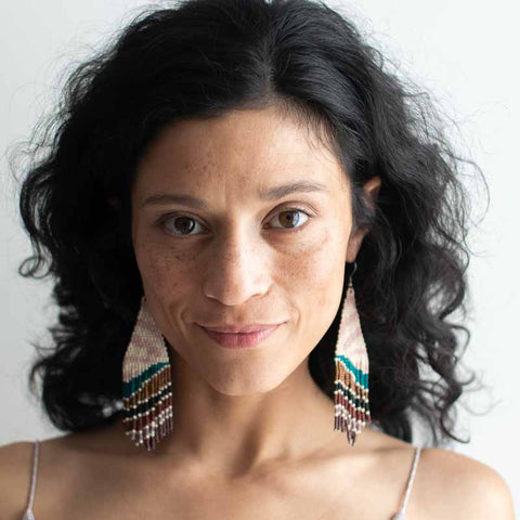 Woman wearing large, colorful beaded earrings against a plain background