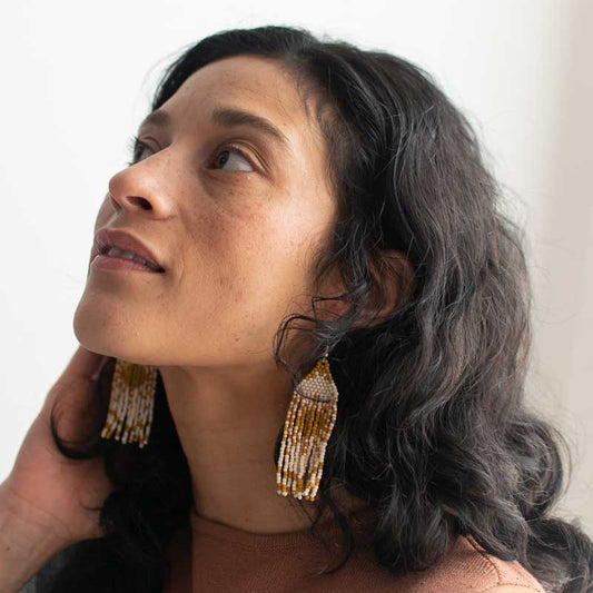 Woman wearing gold beaded earrings with a neutral background