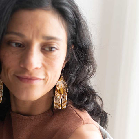 Woman with long dark hair wearing gold earrings, smiling indoors.