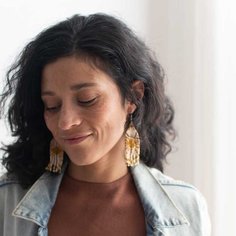 Woman wearing a denim jacket and brown top with gold earrings indoors.