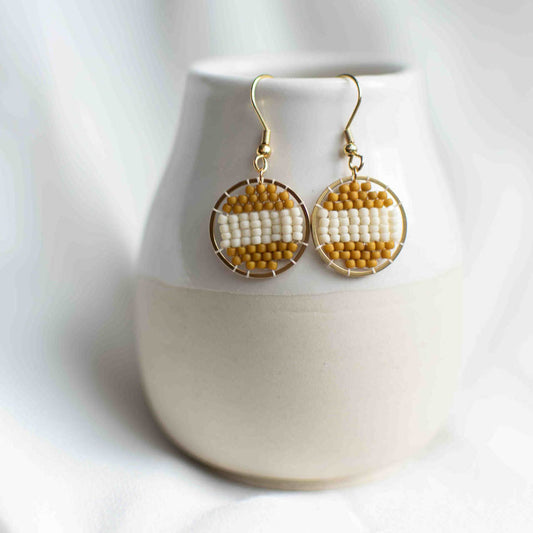Beaded earring in striped mustard and white inside a round gold plated pendant.