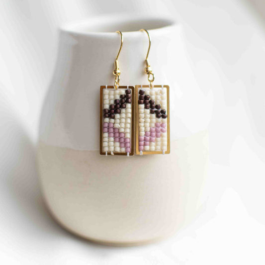 Beaded earrings in purple inside a rectangular gold plated charm.