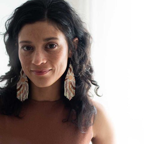 Woman wearing a brown top with tassel earrings against a neutral background