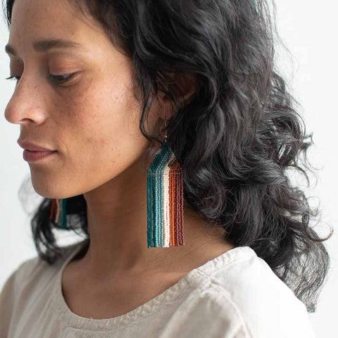 Woman wearing colorful tassel earrings against a neutral background