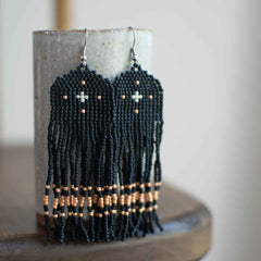 Black beaded earrings with orange accents on a cylindrical stand.