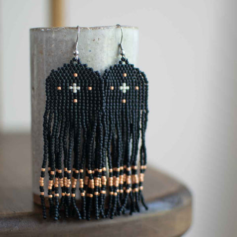 Black beaded earrings with orange accents on a cylindrical stand.