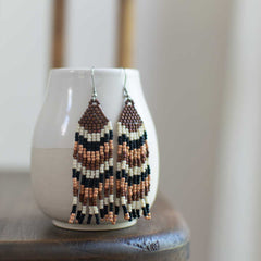 Beaded earrings on a white ceramic vase with a blurred background