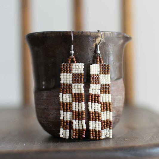 Beaded earrings with a checkered brown and white pattern and fringe.