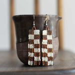 Beaded earrings with a checkered brown and white pattern and fringe.