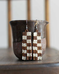 Beaded earrings with a checkered brown and white pattern and fringe.