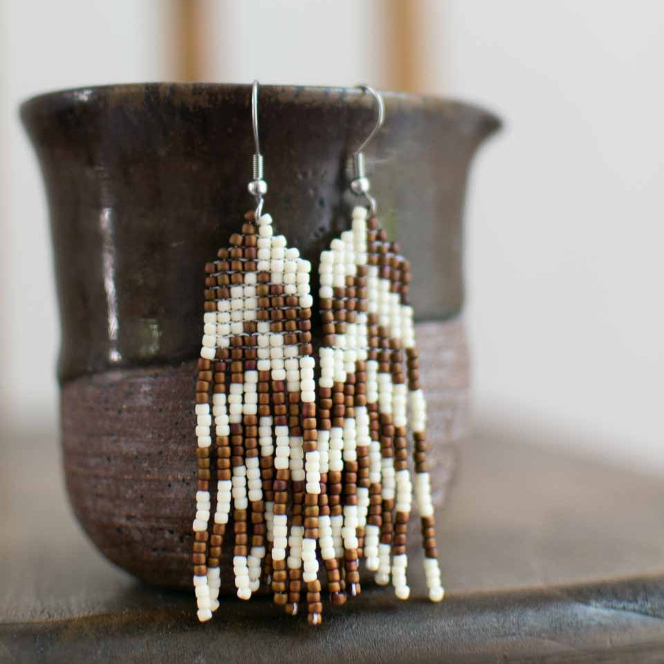 Beaded earrings with brown and white herringbone pattern on a dark surface with a blurred background