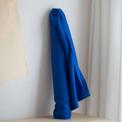 Blue linen roll of fabric on a white wall with a neutral curtain.