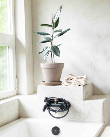 stack of washcloths on bathtub by a plant