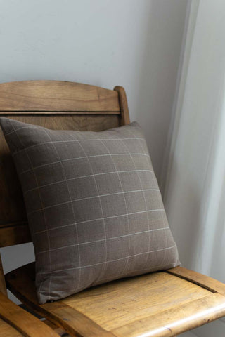 Gray checkered pillow on a wooden chair against a white wall