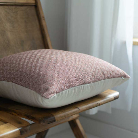 Pink textured pillow on a wooden chair with a white curtain in the background