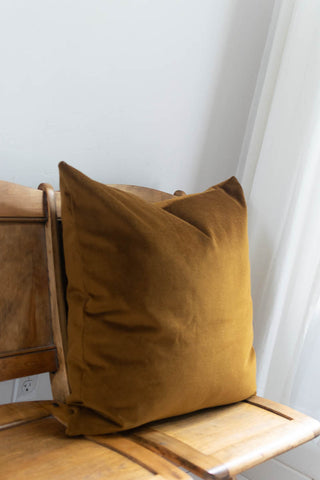 Brown pillow on a wooden chair against a white wall