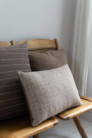 Three patterned cushions on a wooden chair against a neutral wall.
