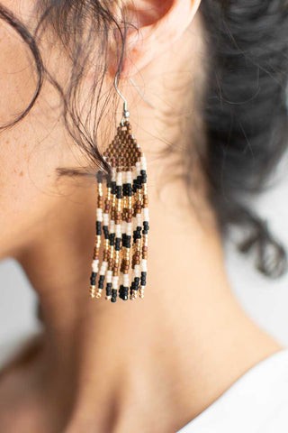 Close-up of a person wearing beaded earrings with a neutral background