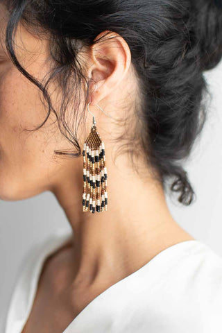 Close-up of a person wearing beaded earrings with a neutral background