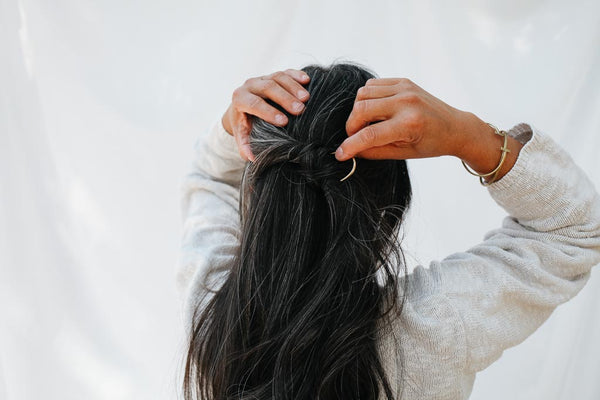 woman putting in hair pin and wearing fair trade bracelet cuffs in matte brass
